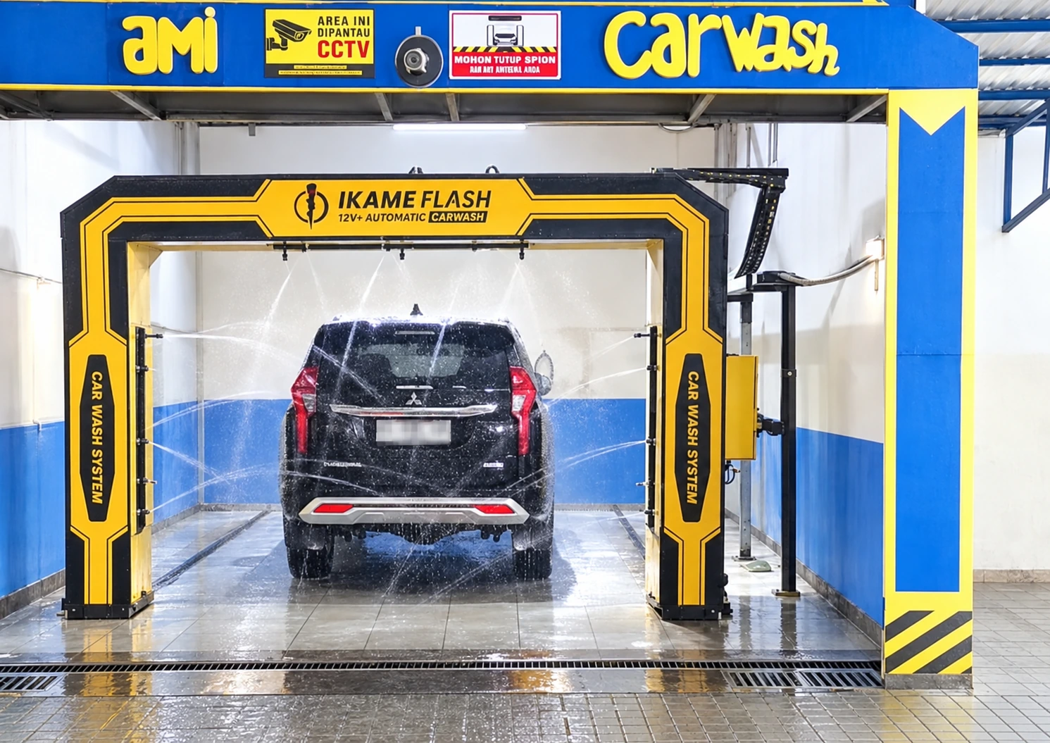 Foto Ami Carwash dengan mesin otomatis kuning dan mobil yang sedang dicuci; orang dihapus, pencahayaan dirapikan, dan nomor polisi dikaburkan melalui penyuntingan AI